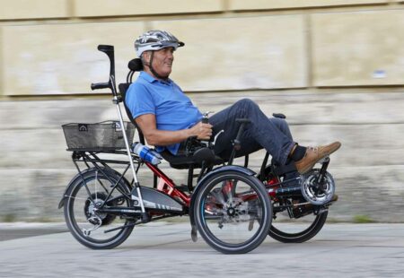 Alter Mann sitzt in einem Seniorendreirad und fährt an einer Mauer entlang